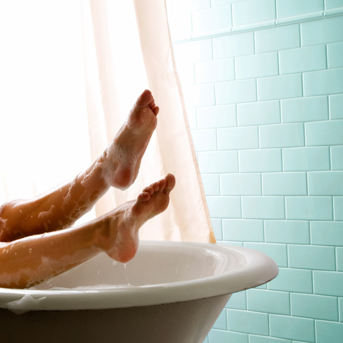 Person’s feet soaked with water and bubbles hanging off the edge of a bath tub